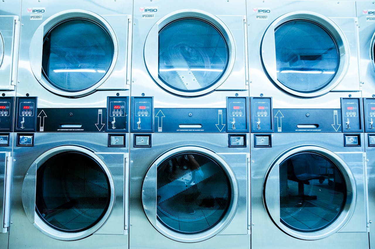about-us-02 A row of modern washing machines in a launderette, showcasing contemporary laundry technology.