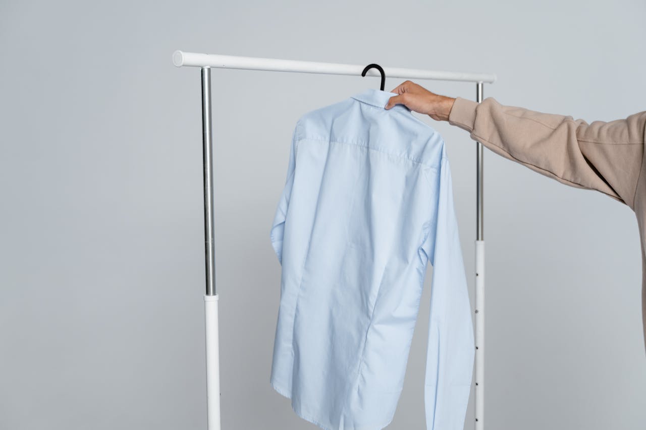 about-us-01 A person holding a blue shirt on a rack against a neutral background.